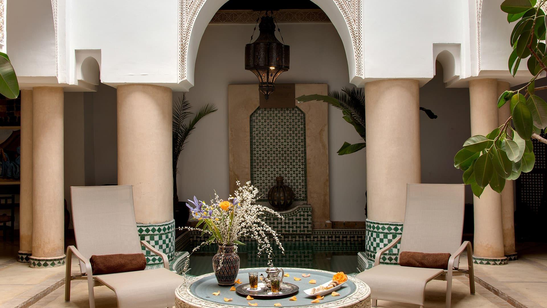 Poolside chairs flank a table with flowers at Angsana Riads Collection - Marrakech, Riad Bab Firdaus.