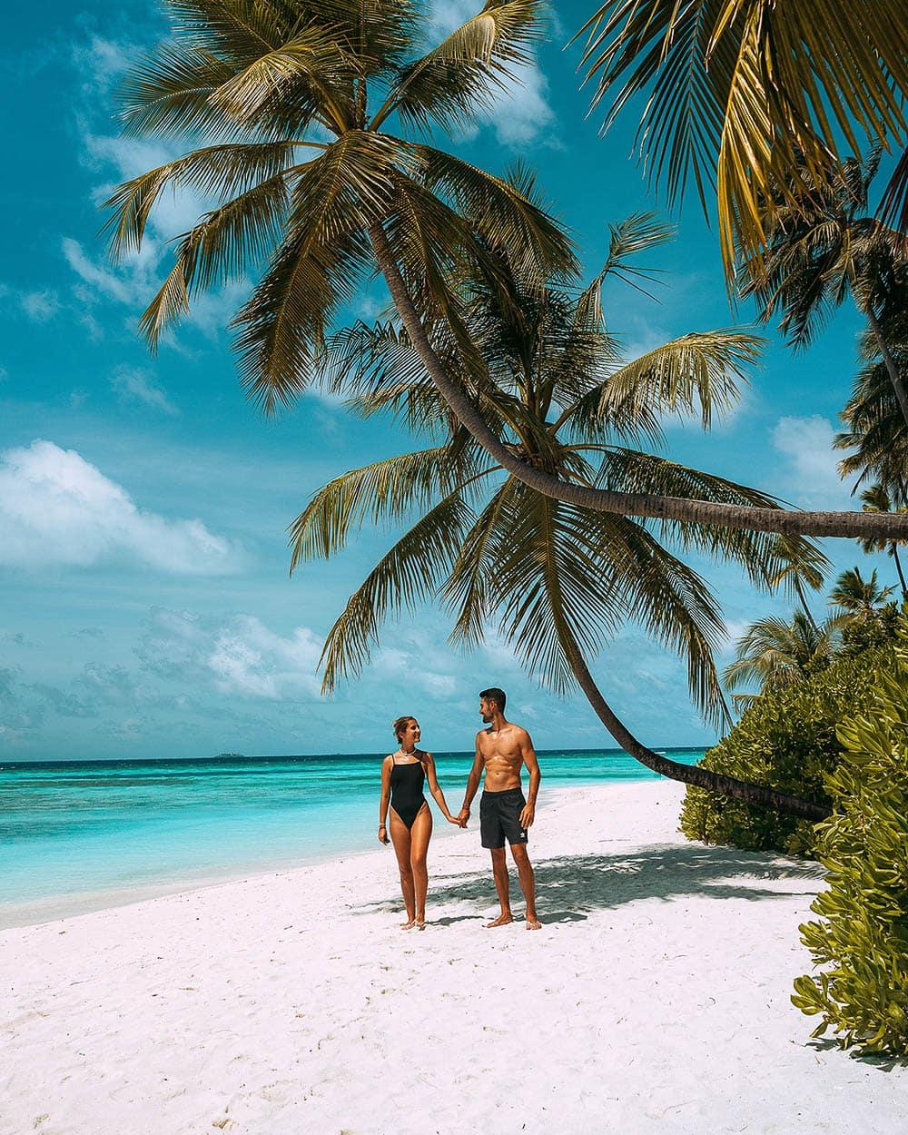 Couple holding hands under a palm tree at Angsana Velavaru